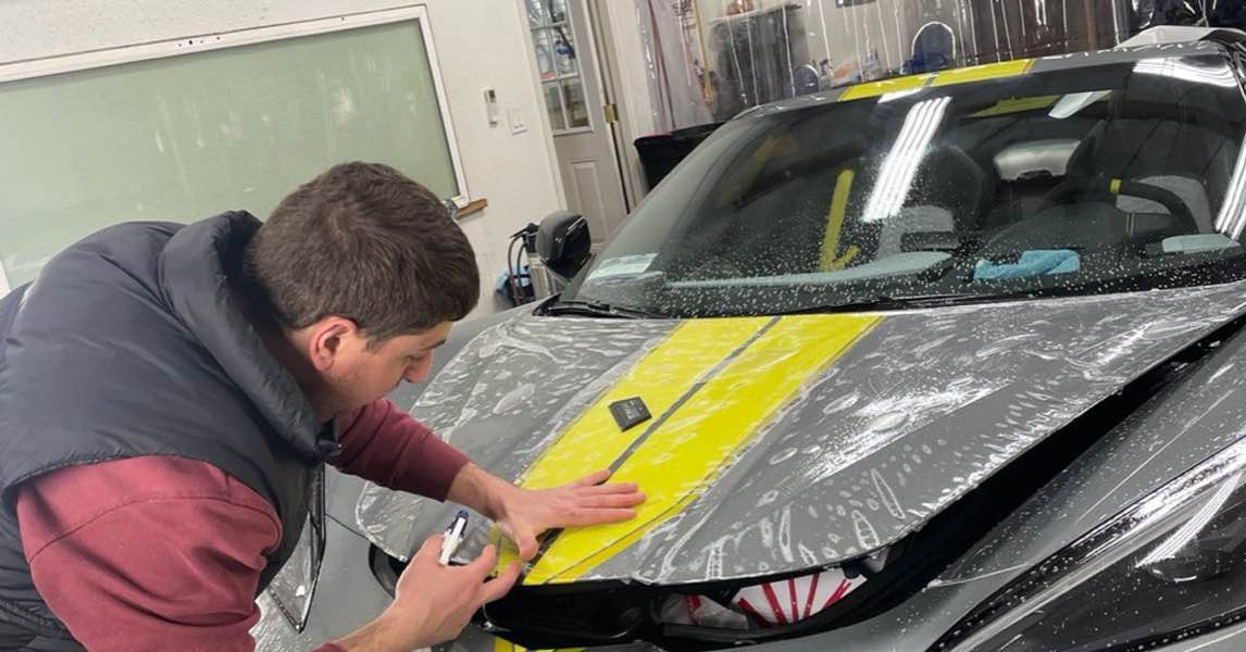 Technician applying paint protection film to a grey sports car with yellow stripes in Gold River, CA.