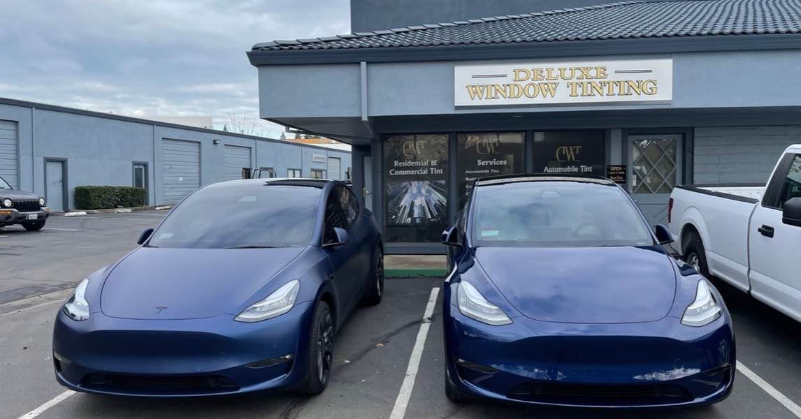 Two blue Tesla Model Y cars with professional window tinting parked in front of Deluxe Window Tinting.